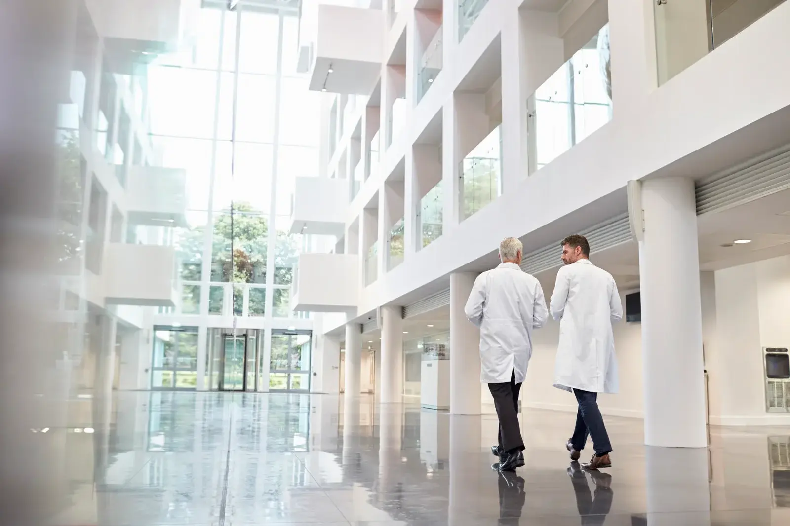 Doctors walking towards a glass door, which is part of the main façade of a hospital, and was put together by façade contractors.  